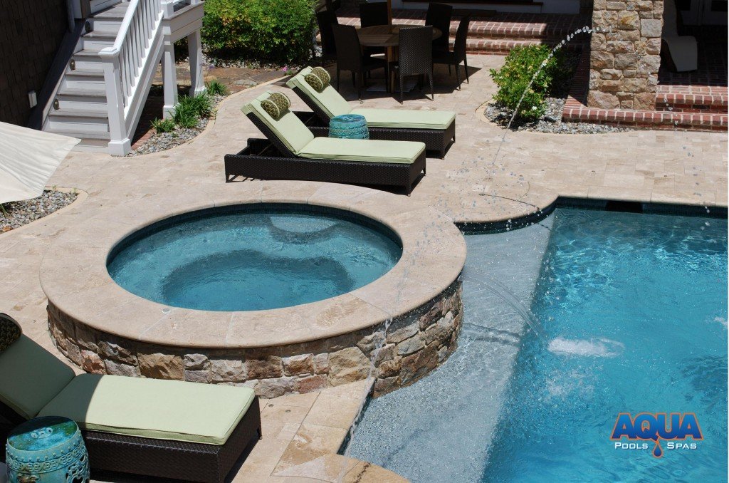 Instead of having a "spill over" into the pool which would dictate the bodies of water (& heat) be shared, we recommend separating the bodies of water.   A waterfall of recirculated pool water can be added to the face of the hot tub to achieve the spillover effect without sharing the water.